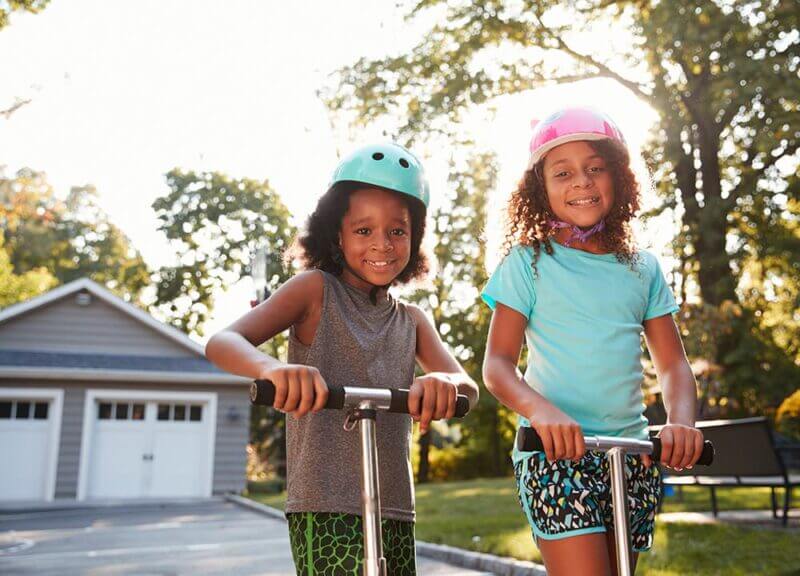 Children on scooters in front of a suburban home