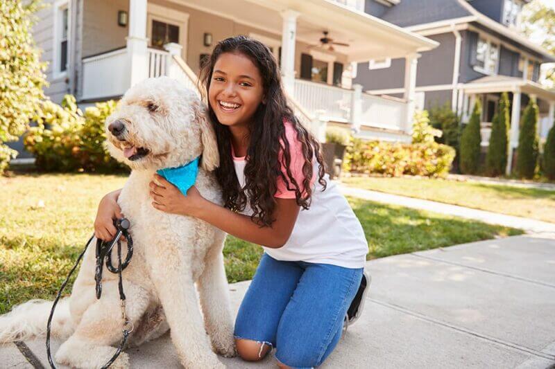 A girl hugs her white dog in front of a suburban home