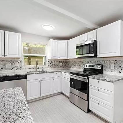 A modern kitchen with white cabinets, granite countertops, and stainless steel appliances